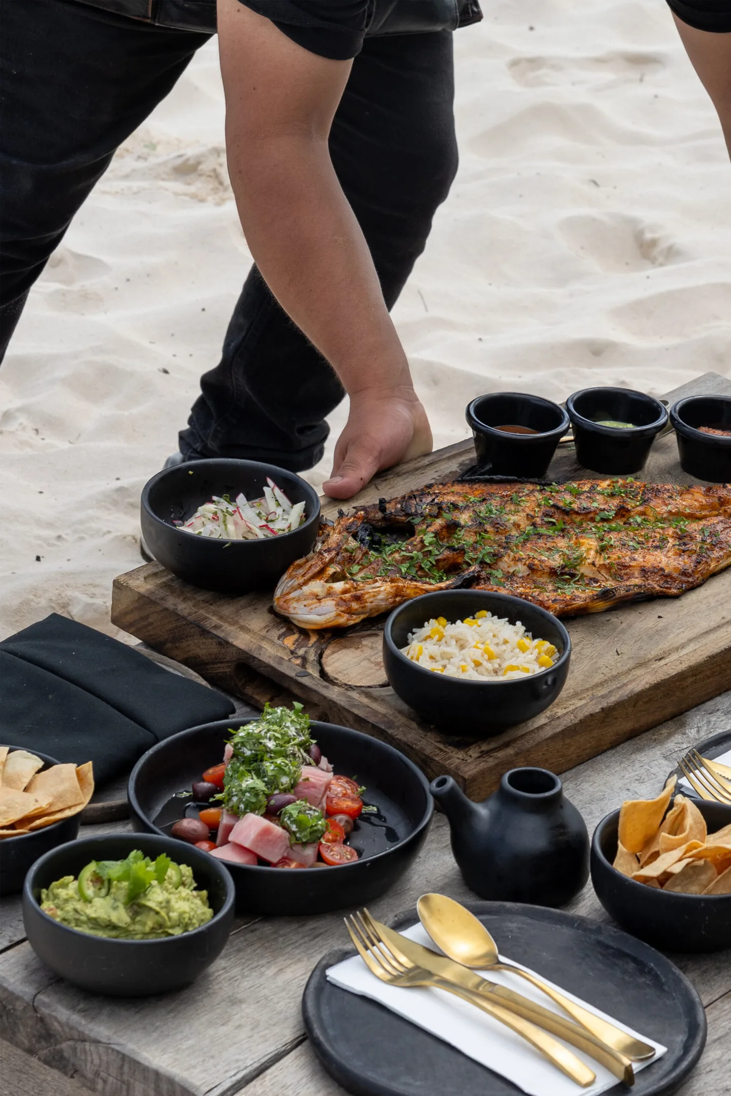 Pescado asado en una tabla de madera con guarniciones sobre la arena