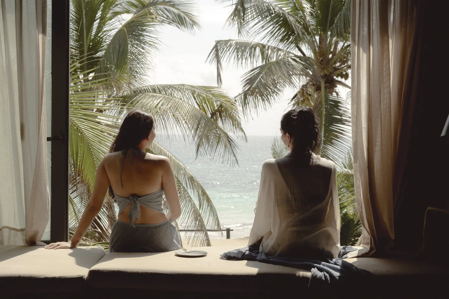 Two women sitting on a window bench overlooking the ocean.