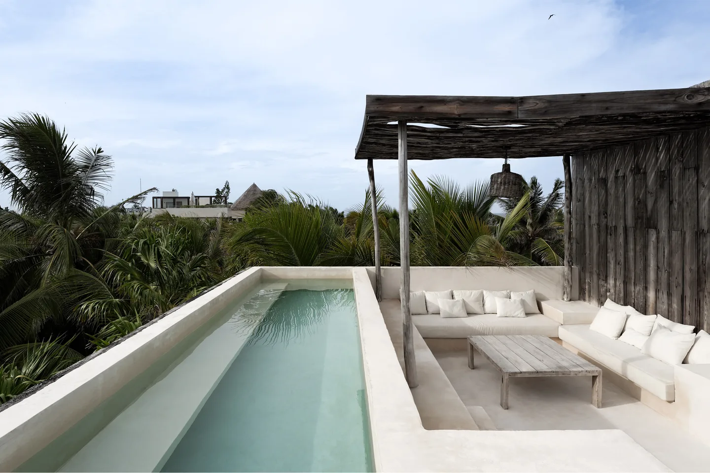 A rooftop with a pool, lounge area, and wooden canopy.